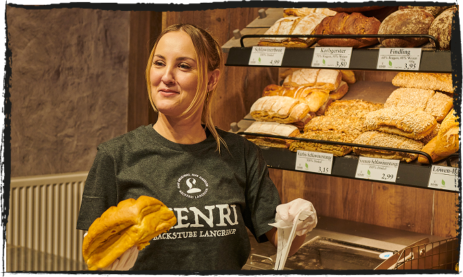 Eine lächelnde Bäckereifachverkäuferin ein packt ein Brot in eine Tüte
